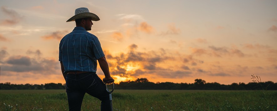 高贵牧场设备经理克拉克·罗伯茨站在日落的牧场上，手里拿着铲子